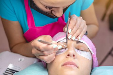 Güzellik salonunda kadın stilist müşteri kirpik uzantısı üzerinde çalışıyor. Kirpiklerin uzamasına yönelik profesyonel bir usta olarak çalışma süreci