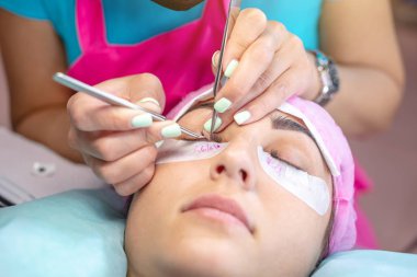 Güzellik salonunda kadın usta müşteri kirpik uzantısı üzerinde çalışıyor. Kirpiklerin uzamasına yönelik profesyonel bir stilist olarak çalışma süreci