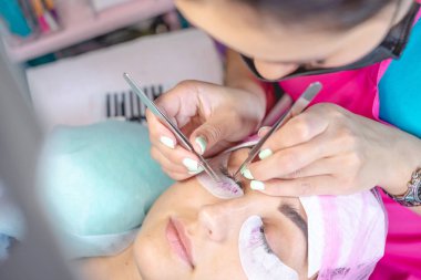 Güzellik salonunda kadın usta müşteri kirpik uzantısı üzerinde çalışıyor. Kirpiklerin uzamasına yönelik profesyonel bir stilist olarak çalışma süreci