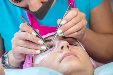 Güzellik salonunda kadın usta müşteri kirpik uzantısı üzerinde çalışıyor. Kirpiklerin uzamasına yönelik profesyonel bir stilist olarak çalışma süreci