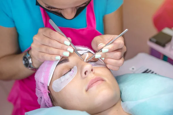 Woman stylist in the beauty salon is working on eyelash extension to the client. Process of working as a professional master for lengthening eyelashes