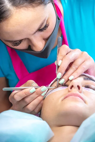 Woman master in the beauty salon is working on eyelash extension to the client. Process of working as a professional stylist for lengthening eyelashes