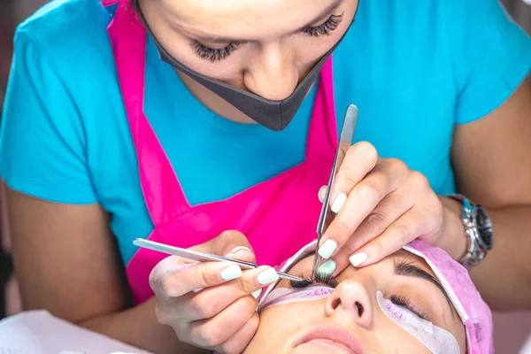Woman master in the beauty salon work on eyelash extension to the client. Process of working as a professional stylist for lengthening eyelashes.