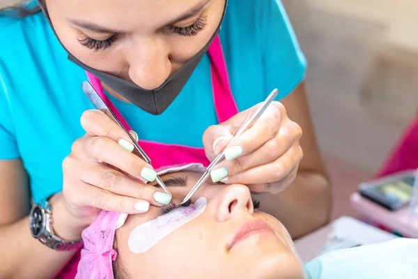 Woman master in the beauty salon work on eyelash extension to the client. Concept of profession in the field of beauty services