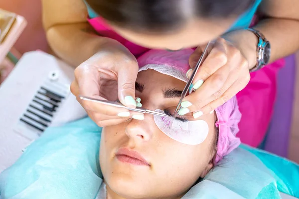 Woman master in the beauty salon work on eyelash extension to the client. Concept of profession in the field of beauty services