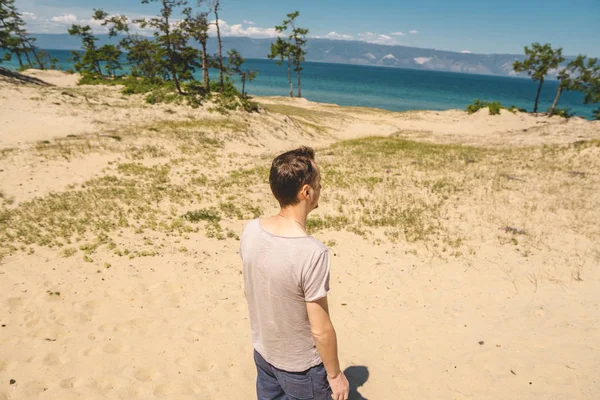 Hombre viajero relajarse en la playa de la isla de Olkhon con vistas al agua del lago y las montañas y el cielo azul — Foto de Stock