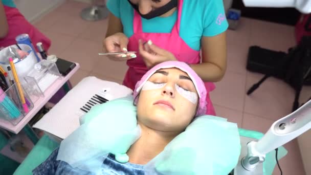 Mujer maestra en el salón de belleza trabajar en la extensión de pestañas para el cliente. Profesión en el campo de los servicios de belleza — Vídeo de stock