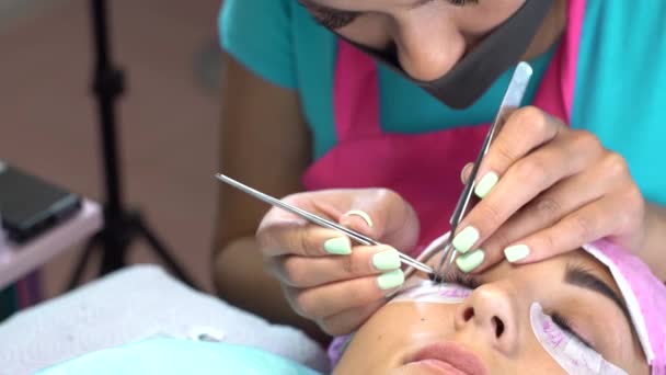 Die Meisterin im Schönheitssalon arbeitet an der Wimpernverlängerung für den Kunden. Beruf im Bereich der Schönheitsdienstleistungen — Stockvideo