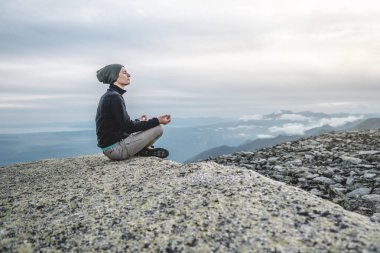 Yazın dağın zirvesinde yoga pozisyonunda oturan yürüyüşçü adam. Dağa uzun bir tırmanıştan sonra meditasyon