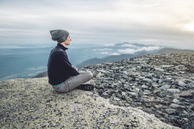 Yazın dağın zirvesinde yoga pozisyonunda oturan yürüyüşçü adam. Dağa uzun bir tırmanıştan sonra meditasyon