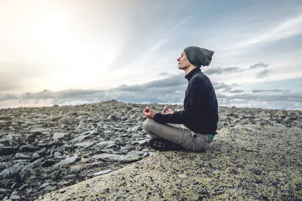Hombre excursionista sentado en una pose de yoga en la cima de la montaña en el verano. Meditación después de una larga escalada en una montaña — Foto de Stock