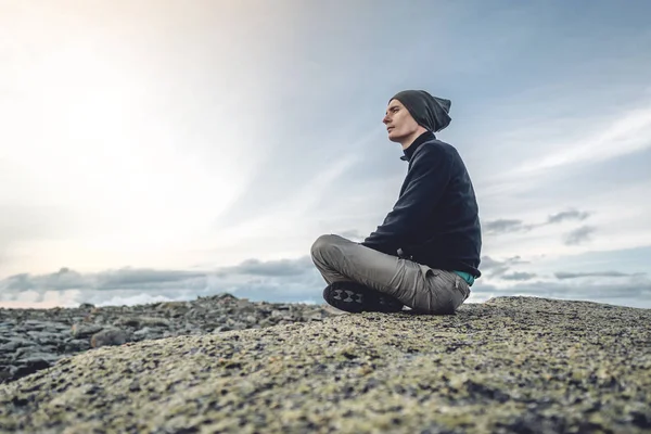 Hombre excursionista sentado en una pose de yoga en la cima de la montaña en el verano. Meditación después de una larga escalada en una montaña — Foto de Stock