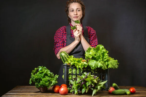 Ung kvinna bonde håller en låda med färska grönsaker och grön sallad. Ekologiska råvaror som odlas på gården. — Stockfoto