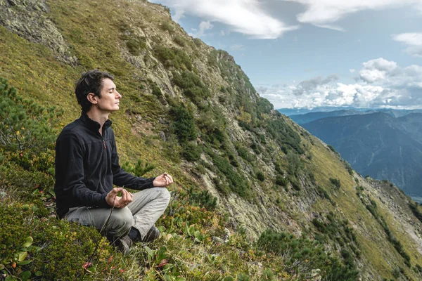 Yazın dağın zirvesinde yoga pozisyonunda oturan yürüyüşçü adam. Dağa uzun bir tırmanıştan sonra meditasyon