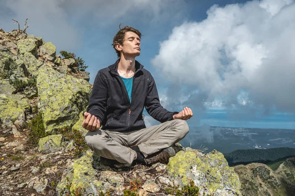 Hombre excursionista sentado en una pose de yoga en la cima de la montaña en el verano. Meditación después de una larga escalada en una montaña — Foto de Stock