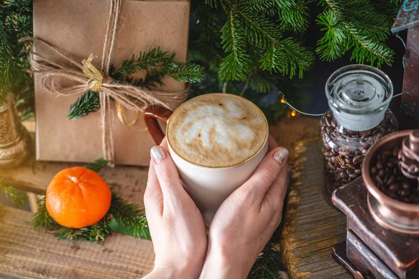 Mug of cappuccino coffee on a wooden background with green branches of a Christmas tree. Warm and cozy from a hot drink. — Stock Photo, Image