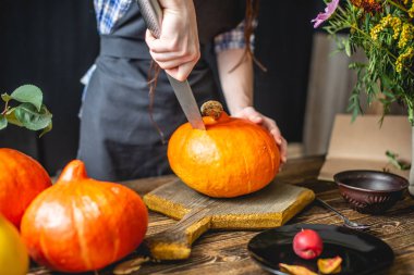 Kadın şef pişirme için hazırlamak için bir portakal kabak temizler. Sarı çiçekler ile rahat bir koyu ahşap mutfakta Sonbahar gıda