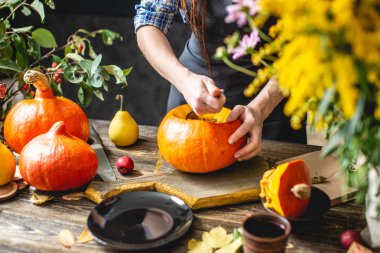 Kadın şef balkabağı çorbası yapmak için portakallı balkabağı temizler. Rahat bir koyu ahşap mutfakta Konsept sonbahar gıda
