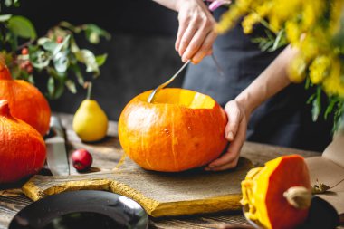 Kadın şef Cadılar Bayramı tatili için oyma için bir portakal balkabağı temizler. Rahat bir koyu ahşap mutfakta Sonbahar gıda