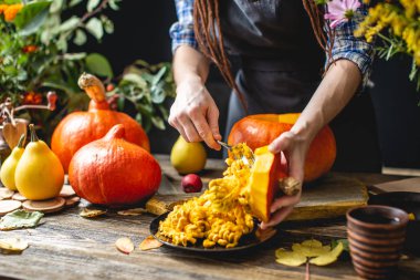 Kadın şef bal ve tarçın ile pişirme için bir portakal kabak pişirme. Koyu ahşap mutfakta konsept sonbahar gıda