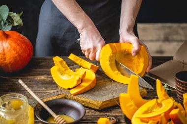Kadın aşçı pişirme için dilimler halinde bir bıçak ile bir portakal kabak keser. Rahat ve karanlık bir mutfakta sonbahar yemekleri. Yakın çekim