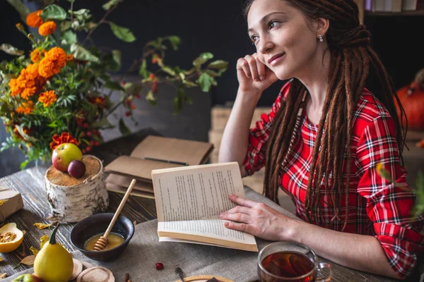 Femme lisant un livre romantique dans une atmosphère chaleureuse profitant de l'ambiance automnale. Table rustique avec fleurs et pile de livres — Photo