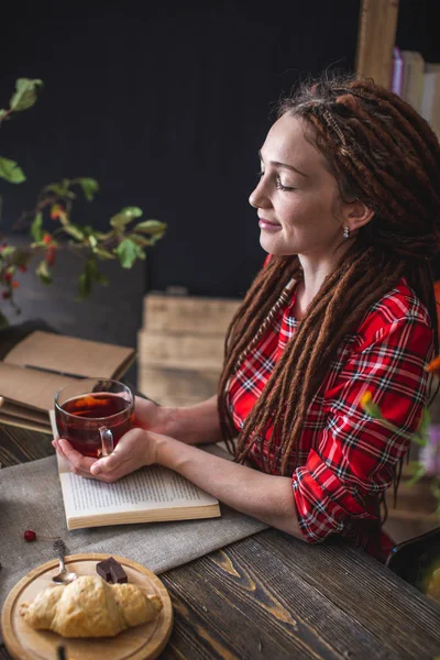 Donna che legge un libro romantico in un'atmosfera accogliente e calda godendo l'atmosfera autunnale. Tavolo rustico con pila di libri — Foto Stock