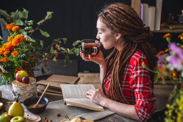 Donna che legge un libro romantico in un'atmosfera accogliente e calda godendo l'atmosfera autunnale. Tavolo rustico con pila di libri — Foto Stock