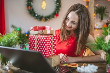 Güzel bir kadın elinde bir hediye kutusu tutuyor ve dizüstü bilgisayardan sipariş veriyor. Noel tatili için online alışveriş.
