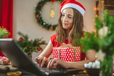 Kadının elinde bir hediye kutusu var ve dizüstü bilgisayardan sipariş veriyor. Noel tatili için online alışveriş.