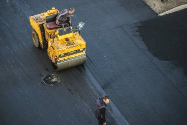 İşçiler sıcak bitumen kullanarak yeni bir asfalt kaplama sererler. Ağır makineler ve kaldırımlar. Üst görünüm