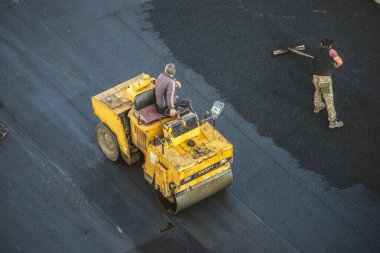 İşçiler sıcak bitumen kullanarak yeni bir asfalt kaplama sererler. Ağır makineler ve kaldırımlar. Üst görünüm