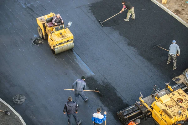 İşçiler sıcak bitumen kullanarak yeni bir asfalt kaplama sererler. Ağır makineler ve kaldırımlar. Üst görünüm