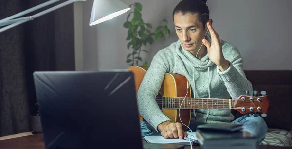 年轻的男歌手正在学习如何在网上用笔记本电脑弹吉他 晚上在家里房间的灯旁边弹 — 图库照片