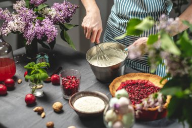 Ev yapımı yabanmersinli turta yapıyorum. Kadın bir pasta şefi ekşi krema çırpıyor. Parlak malzemeli masa, bahar stili, çiçekli.
