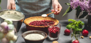 Ev yapımı yabanmersinli turta yapıyorum. Kadın bir pasta şefi, yaban mersinli fırında pişmiş tarta ekşi krema ekliyor. Parlak malzemeli masa, bahar stili, çiçekli.