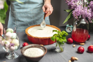 Ev yapımı yabanmersinli turta yapıyorum. Kadın bir pasta şefi, yaban mersinli fırında pişmiş tarta ekşi krema ekliyor. Parlak malzemeli masa, bahar stili, çiçekli.