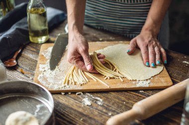 Bir kadın ev yapımı erişte yapmak için çiğ hamuru bıçakla kesiyor. Sıcak bir atmosferde el yapımı makarna pişirme süreci kavramı