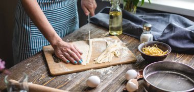 Bir kadın ev yapımı erişte yapmak için çiğ hamuru bıçakla kesiyor. Sıcak bir atmosferde el yapımı makarna pişirme süreci kavramı