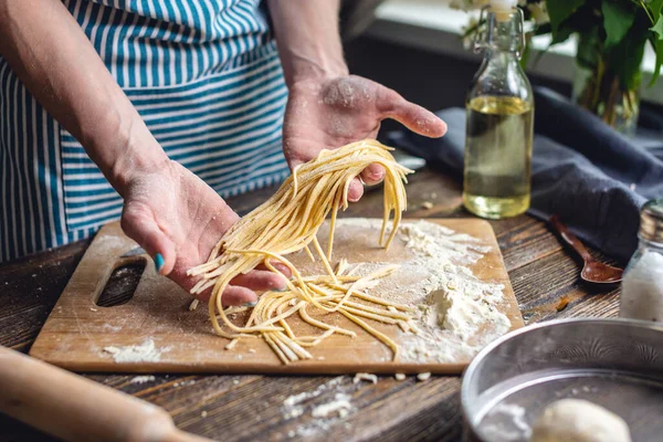 Kadın elinde çiğ taze erişteyi dikkatlice tutuyor. Sıcak bir atmosferde el yapımı makarna pişirme süreci kavramı