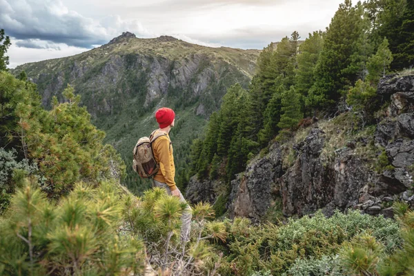 Turista Batohem Červeným Kloboukem Stojí Okraji Útesu Dívá Hory Koncept — Stock fotografie