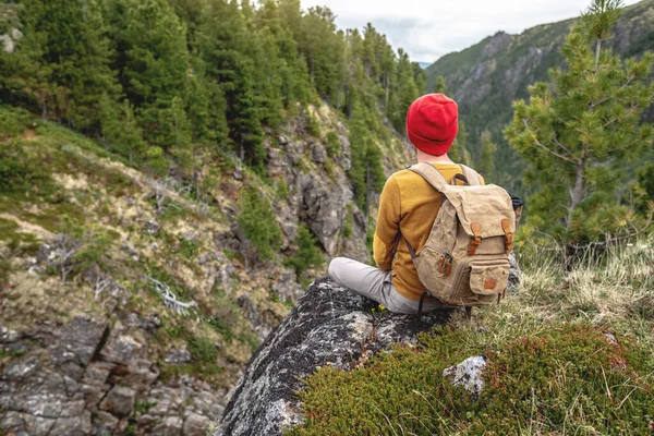 Turista Batohem Červeným Kloboukem Sedí Okraji Útesu Dívá Hory Koncept — Stock fotografie