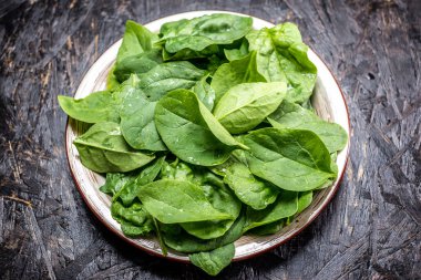 Koyu arkaplandaki tabakta taze ıspanak yaprakları. Sağlıklı vejetaryen yemekleri. Yukarıdan görünüşü.
