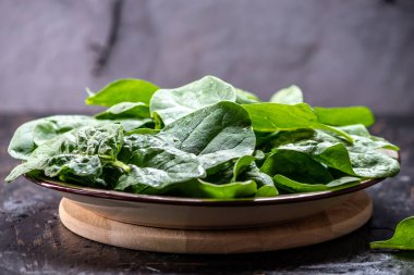 Koyu arkaplandaki tabakta taze ıspanak yaprakları. Sağlıklı vejetaryen yemekleri
