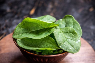 Koyu arkaplandaki tabakta taze ıspanak yaprakları. Sağlıklı vejetaryen yemekleri