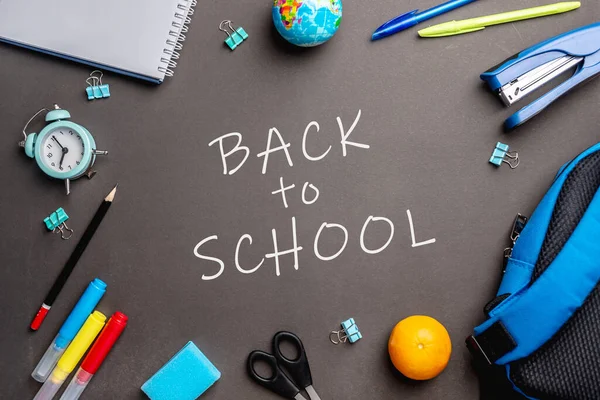 Kırtasiye malzemesi, siyah arka planda okula dönüş kelimesinin etrafında. Üst görünüm.