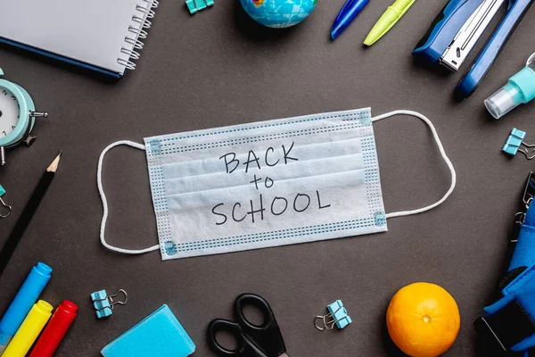 Stationery school supplies around the medical mask on black background. Top view. Concept of back to school.