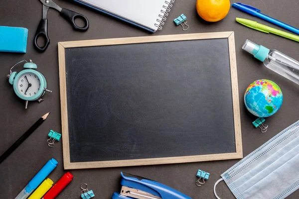 Stationery school supplies, medical mask and antiseptic on a black background. Top view and copy space. Concept of back to school