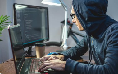 Kapüşonlu bir bilgisayar korsanı dizüstü bilgisayarda virüs kodları programlıyor. İnternet dolandırıcılığı ve kişisel veri hackleme kavramı