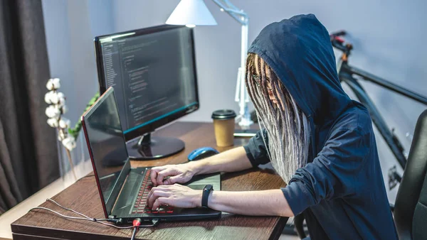 Kapüşonlu bir kadın bilgisayar korsanı dizüstü bilgisayarında virüs kodu programlıyor. İnternet dolandırıcılığı ve kişisel veri hackleme kavramı